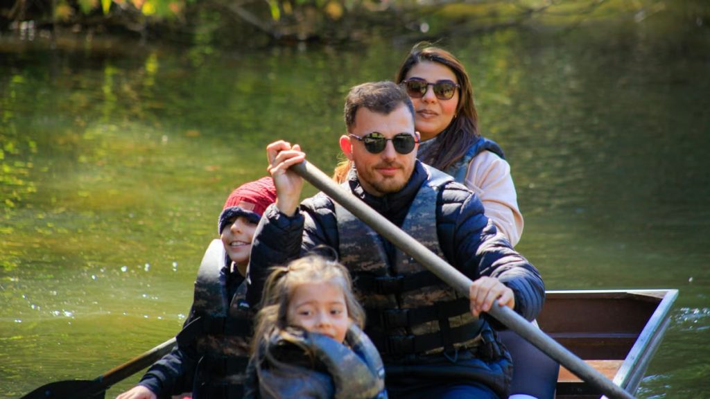 A family of four rowing a canoe on a serene lake during a sunny day, enjoying an outdoor adventure.